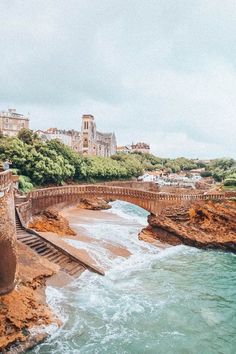 an old stone bridge over the ocean with waves crashing in front of it and buildings on the other side