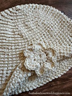 a crocheted hat with a flower on it sitting on top of a wooden table