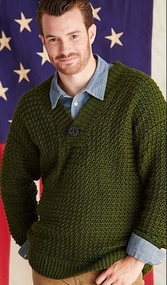 a man standing in front of an american flag wearing a green sweater and khaki pants