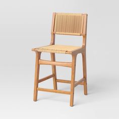 a wooden chair with wicker seat and back rests on a white surface, in front of a gray background