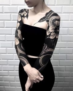 a woman with black and grey tattoos on her arm is standing in front of a white brick wall