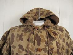 "Vintage 1940s hunting jacket, hooded coat. Made of brown camouflage cotton. Has a corduroy zippered split hood, chinstrap, four pockets, back game pouch, cotton flannel lined cowl and a button front. No label. Size large. Actual measurements are: 52\" at the chest 52\" at the waist 21\" shoulder seam to shoulder seam 22\" shoulder seam to end of cuff 26.5\" overall length In very good condition, nice natural fade." Camo Hunting Jacket, 1940s Jacket, Hunting Jacket, Camouflage Jacket, Hunting Jackets, Jacket Vintage, Hooded Coat, Vintage Jacket, Cotton Flannel