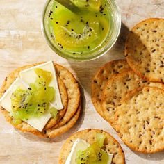 crackers with kiwi fruit and cheese on them next to a jar of pickles