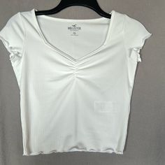 Hollister White Tee - Brand New Without Tags!! V-Neck Ruched Chest Lettuce Edge On Sleeve And Bottom Hem. Ribbed Detail Soft Material 88% Polyester / 12% Elastane Size: Xs Color: White Condition: Brand New!! Never Worn Or Washed. Casual White Fitted V-neck Top, Casual White Stretch V-neck Top, Ribbed V-neck T-shirt For Summer, Casual Fitted White V-neck Top, Casual Fitted V-neck Top, Casual Ribbed V-neck Top, Clothing Pieces, Thrift Finds, Fairytale Art