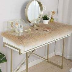 a vanity table with a mirror, plant and other items on it in front of a white wall