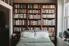 a bed sitting in front of a book shelf filled with books next to a window