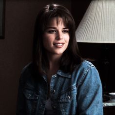 a woman sitting next to a lamp in a room with a blue jean jacket on