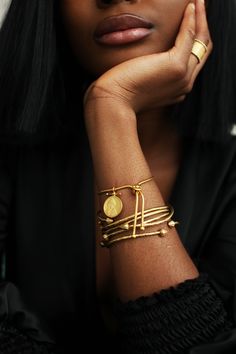 a woman with her hand on her chin wearing gold bracelets and a black shirt