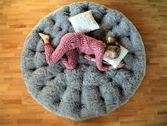 a woman laying on top of a gray round bed with pillows and blankets around her