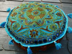 a decorative round cushion with tassels on the top sitting on a stone floor