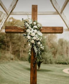 a cross decorated with white flowers and greenery for a wedding at the farm house