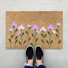 someone standing in front of a door mat with flowers painted on it