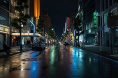 an empty city street at night with cars parked on the side walk and buildings in the background