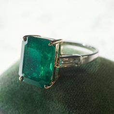 This stunning ring features a GIA certified 4.23 carat step cut emerald and diamond accents in 14 karat yellow gold and platinum. The impressive center stone features a rich sea green hue and is set in a four pronged 14 karat yellow gold basket. With elongated facets and tapered corners, the emerald is accented by two (2) .25 carat baguette cut diamonds. The diamonds are near colorless and visually complement the shimmering platinum band. This fabulous right hand ring features a subtle two-toned Gold Basket, Emerald Ring Vintage, Right Hand Ring, Emerald And Diamond Ring, Antique Diamond Rings, Emerald Diamond Ring, Right Hand Rings, Hand Ring, Step Cut