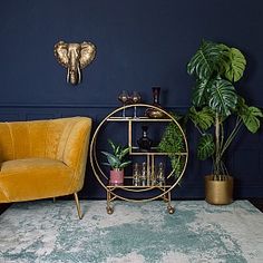 a gold shelf with plants and glasses on it next to a yellow chair in front of a blue wall