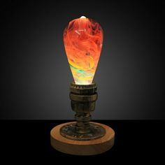 an orange and yellow lamp sitting on top of a wooden stand next to a black background