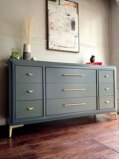 a large gray dresser with gold handles in a living room next to a painting on the wall