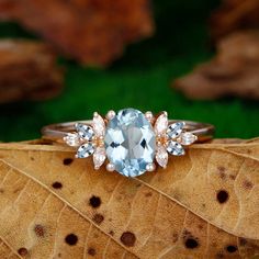 a ring with an aqua blue topaz surrounded by white and rose gold accents sits on a leaf