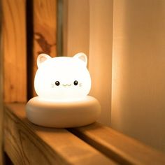 a white cat lamp sitting on top of a wooden shelf next to a window sill