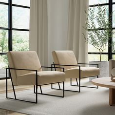 two beige chairs sitting in front of large windows next to a table with a vase on it