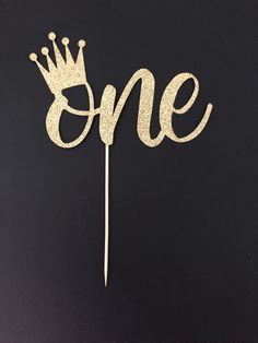 a cake topper with the word one written in gold glitter and a crown on it