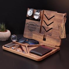 a wooden case with sunglasses, wallet and other items in it next to a potted plant