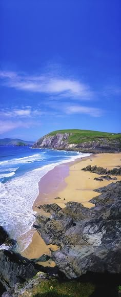 the beach is surrounded by large rocks and blue water with waves coming in to shore