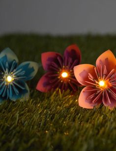 three paper flowers sitting in the grass with their lights on