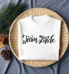 a t - shirt that says team bride on it next to pine cones and an evergreen branch