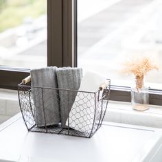 two towels are sitting in a wire basket on a window sill next to a vase with flowers