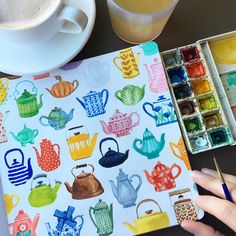 a person holding a paintbrush next to a drawing book with teapots and cups on it