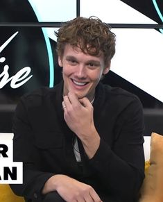 a young man sitting on top of a yellow couch next to a white and black sign