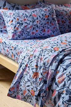 a bed with blue and orange floral bedspread on top of wooden flooring