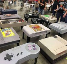 several video game console tables are arranged in a room with people standing around and looking at them