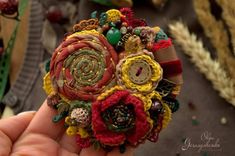 a hand holding a small brooch made out of yarn and fabric with buttons on it