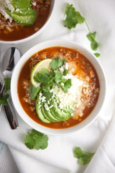 two bowls of chili soup with avocado and shredded cheese on the top one