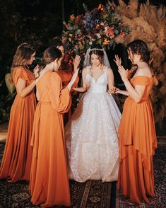 the bride is surrounded by her four bridesmaids in orange dresses and veils