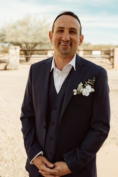 a man in a suit and flowered boutonniere smiles at the camera