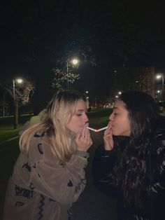 two women standing next to each other in the dark, one is biting into another woman's mouth