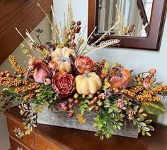 a vase filled with flowers and leaves on top of a wooden dresser next to a mirror