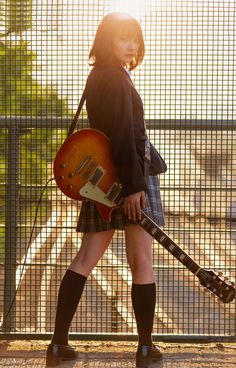 a woman with a guitar in her hand is walking down the street while holding an electric guitar