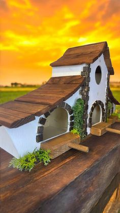 a white birdhouse sitting on top of a wooden fence in front of a sunset