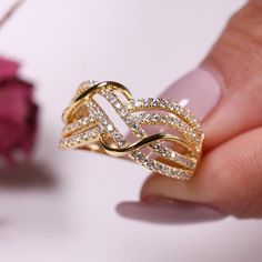 a woman's hand holding a gold ring with diamonds on it and a rose in the background