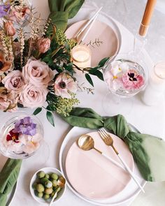 the table is set with pink flowers and greenery, candles, plates and utensils