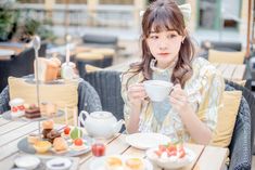 a woman sitting at a table holding a cup and saucer in front of her