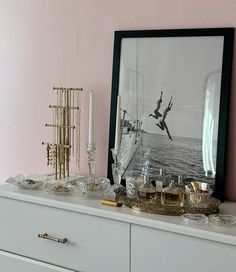 a white dresser topped with lots of glassware and bottles next to a framed photograph