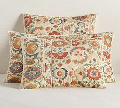 two pillows on a bed with white sheets and floral print in the middle, one is made out of linen