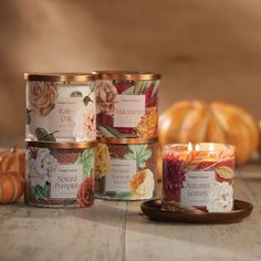 three candles sitting next to each other on top of a wooden table with pumpkins in the background