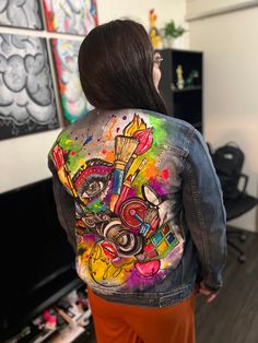 a woman wearing a jean jacket with colorful paint splattered on the back and sides