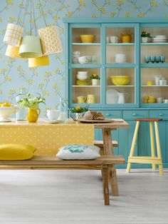 a dining room with blue cabinets and yellow accents on the walls, along with white dishes